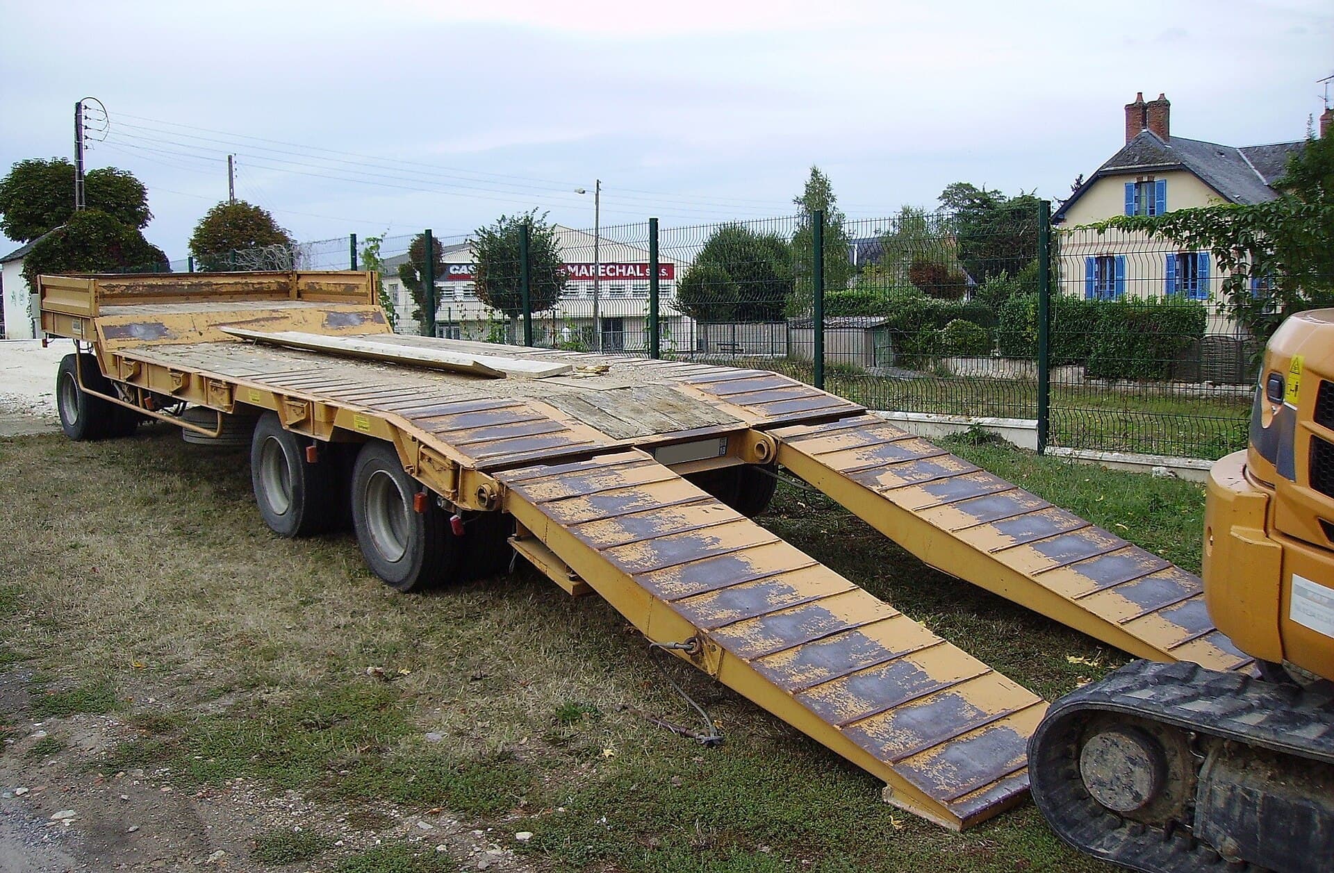 Excavator loaded on a low machinery trailer with ramps and tie-down chains