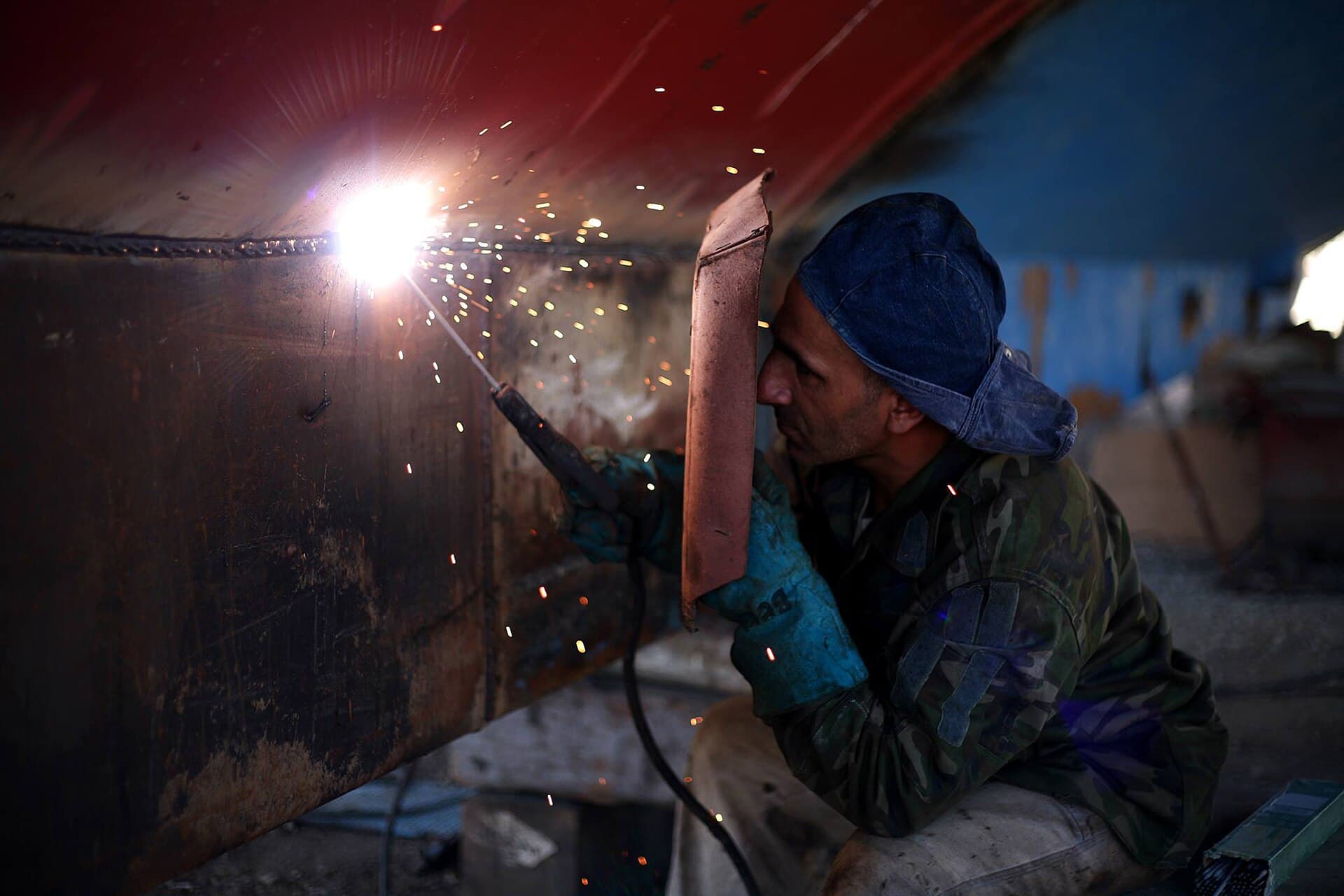Welder working on steel in a workshop with sparks falling from the torch